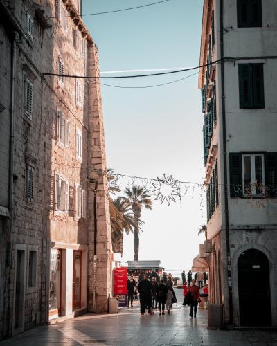 A bustling pedestrian walkway in Split, Croatia, featuring historic stone buildings and palm trees under a clear sky.