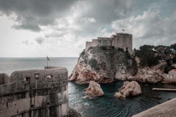 Majestic view of Dubrovnik's medieval forts and rocky coast under dramatic skies.
