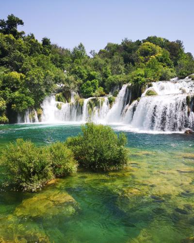 Scenic view of a lush waterfall in Krka National Park, Croatia, surrounded by vibrant greenery.