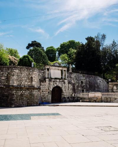 Explore the ancient stone gateway in Queen Jelena Madijevka Park, Zadar, with vibrant greenery and clear skies.